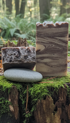 Two soap bars with a woodgrain pattern on a mossy log in a forest setting